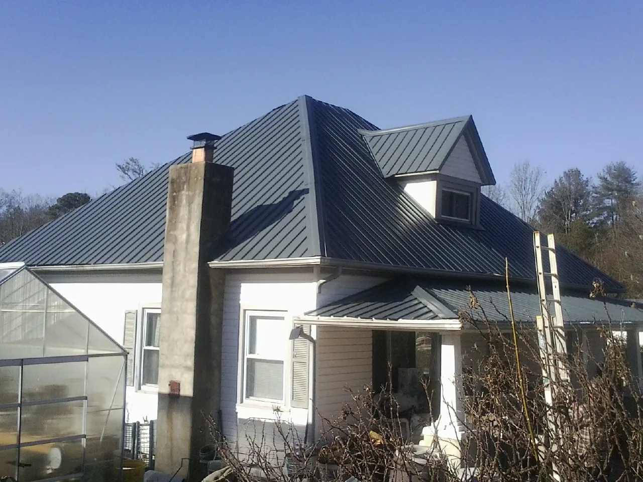 Dark blue standing seam metal roof on a white farmhouse with dormer — Slate & Tile Roof Repair by Roofing Brothers in Stanwood