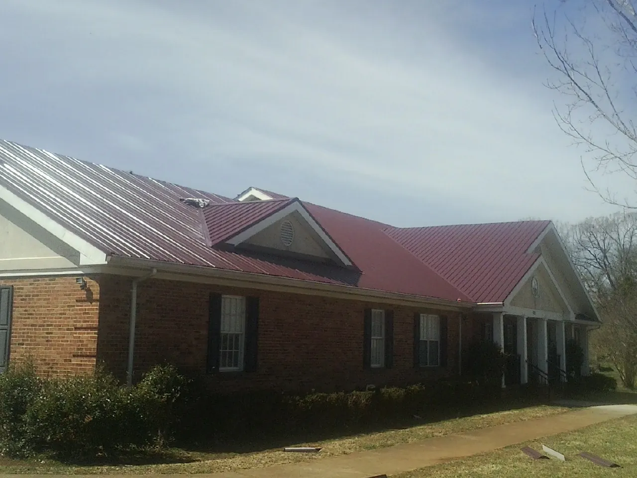 Red metal roof with gabled entries on a long brick building, from a Hail Damage Roof Repair job in Stanwood